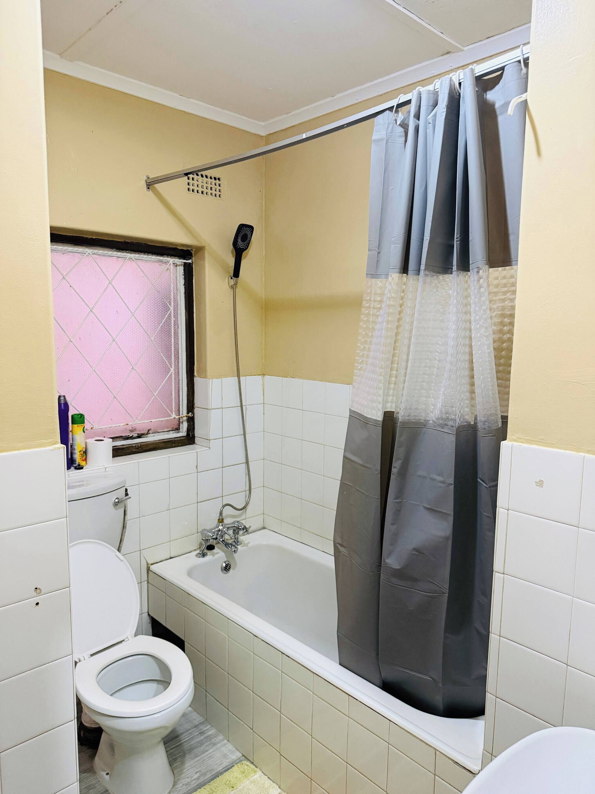 A bathroom with a toilet, bathtub, shower, and a window with a pink mesh screen.