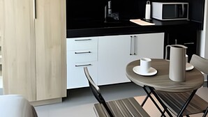 A modern kitchen with white cabinetry, a black countertop, and a dining area with a table and chairs. - Flat Beira mar João Pessoa (João Pessoa)