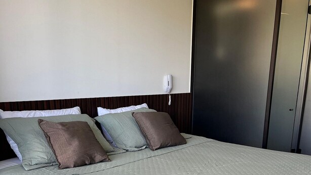 A neatly made bed with a quilted cover and pillows, a bedside telephone, and a wall-mounted air conditioning unit. - Flat Beira mar João Pessoa (João Pessoa)