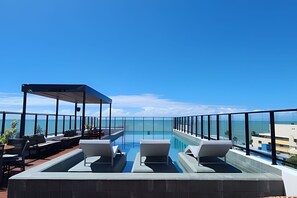 Una piscina infinita en la azotea con sillones de descanso y un área de estar cubierta, con vista al océano.