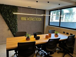Un salón de conferencias con una larga mesa, sillas negras, plantas en macetas y una pared con un cartel que dice 'GATE WORKSTATION'.