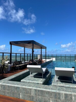 A rooftop infinity pool with lounge chairs and a covered seating area, overlooking the ocean. - Flat Beira mar João Pessoa (João Pessoa)