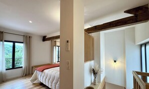 A bedroom with a bed, a window, a wall-mounted light, and a wooden ceiling beam. - Duplex with pool and AC - 2 guests (Savignac-de-Miremont)