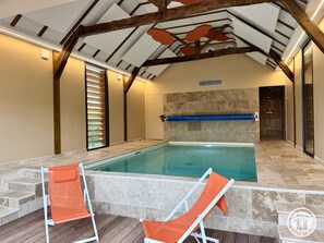 An indoor swimming pool with a wooden ceiling, stone walls, and two orange lounge chairs. - Duplex with pool and AC - 2 guests (Savignac-de-Miremont)