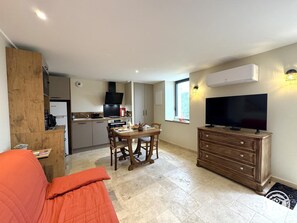 A compact living space with a kitchenette, a dining area, a television, and a sofa. - Duplex with pool and AC - 2 guests (Savignac-de-Miremont)