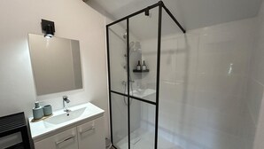 Moderni kylpyhuone, jossa on lasinen suihkuseinä, valkoinen pesuallas ja suuri peili.