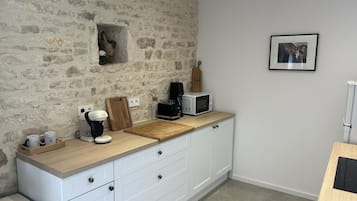 Een keuken met een stenen muur, witte kasten, een houten aanrecht, een koffiezetapparaat, een magnetron, en een lijst met een afbeelding aan de muur.