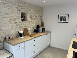 A kitchen with a stone wall, white cabinets, a wooden countertop, a coffee maker, a microwave, and a framed picture on the wall.