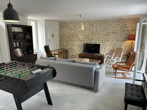 A living room with a foosball table, a sofa, a television, and a stone wall.