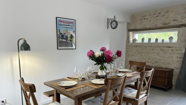 A dining area with a wooden table set for four, chairs with cushioned seats, a vase with flowers, a wall clock, and a poster on the wall. - House with private pool, pets allowed - 6 guests (Courcôme)