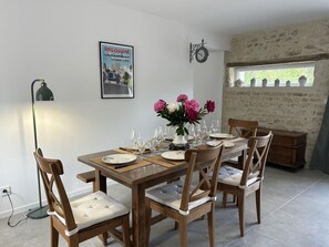 A dining area with a wooden table set for four, chairs with cushioned seats, a vase with flowers, a wall clock, and a poster on the wall.