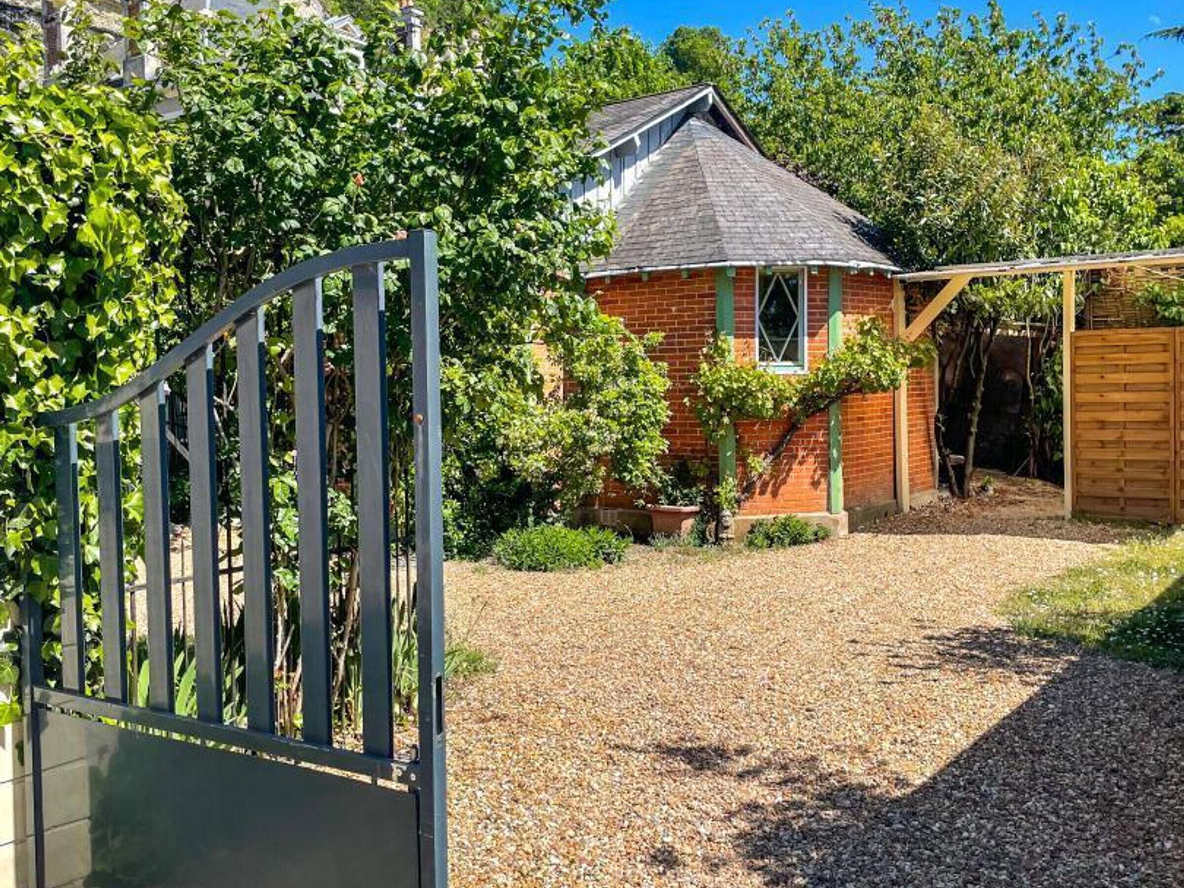 Une maison en briques avec un toit en pente, une allée gravillonnée et une clôture en bois.