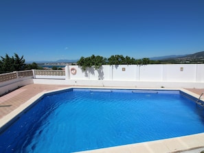 A clear blue swimming pool with a white wall and a lifebuoy, surrounded by a white fence and greenery. - Apartment with AC, sea view - 4 guests (Roses)