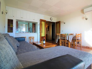 A living room with a sofa, dining table, chairs, and a kitchen area. - Apartment with AC, sea view - 4 guests (Roses)