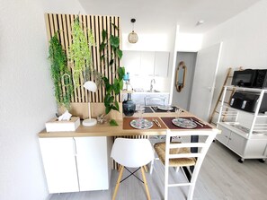 Eine moderne Küche mit einer Wand aus Holzlatten, weißen Schränken, einem für vier Personen gedeckten Esstisch und einem weißen Stuhl.