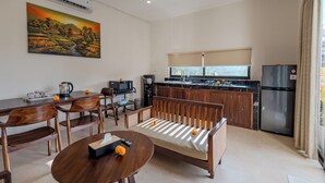 A modern kitchen with a refrigerator, microwave, and stove. There is a dining area with wooden furniture and a painting on the wall. - Shrivatsa Home Villa (Munggu)