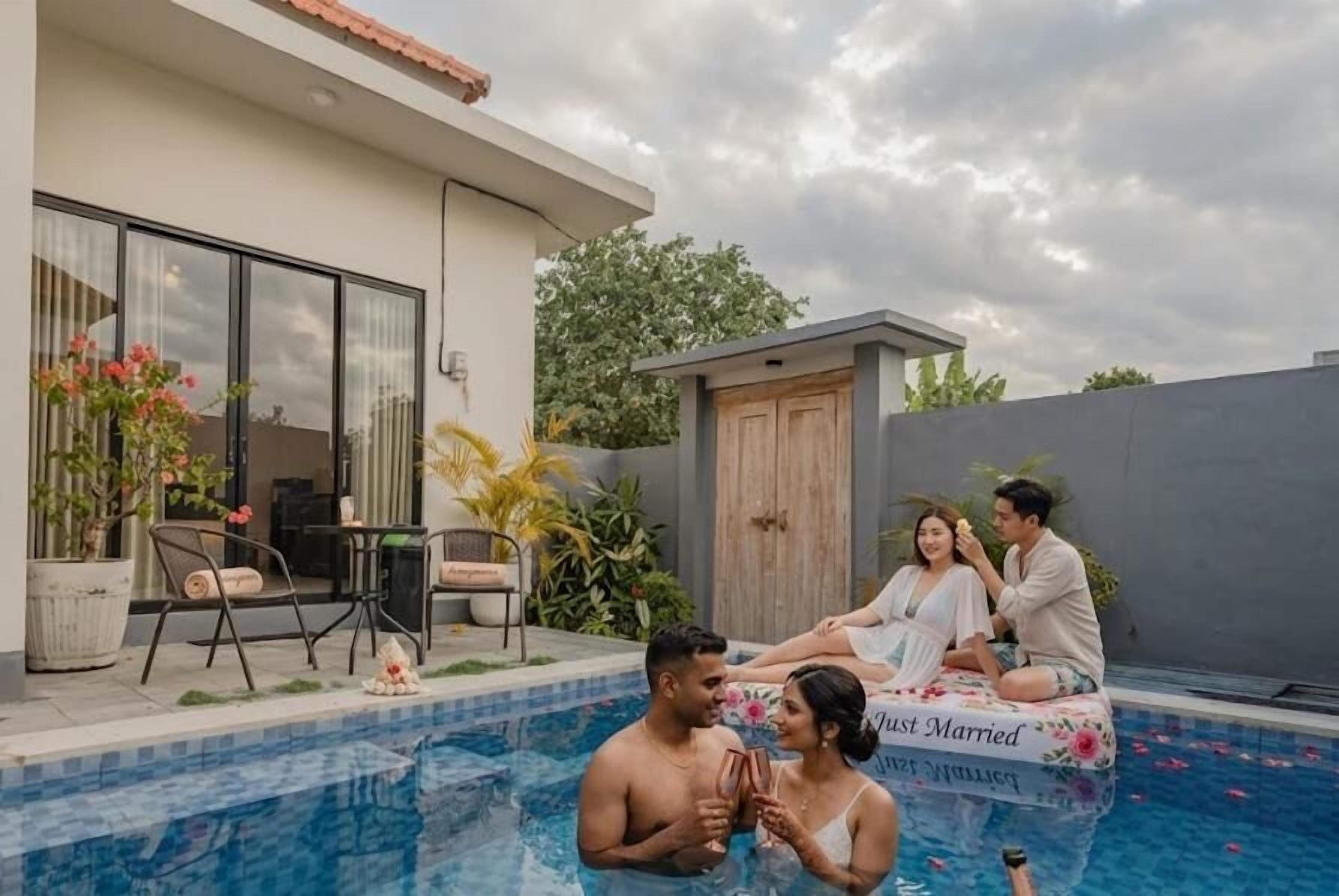 Un área de piscina con una casa moderna, mobiliario exterior y una pareja sentada en un flotador.