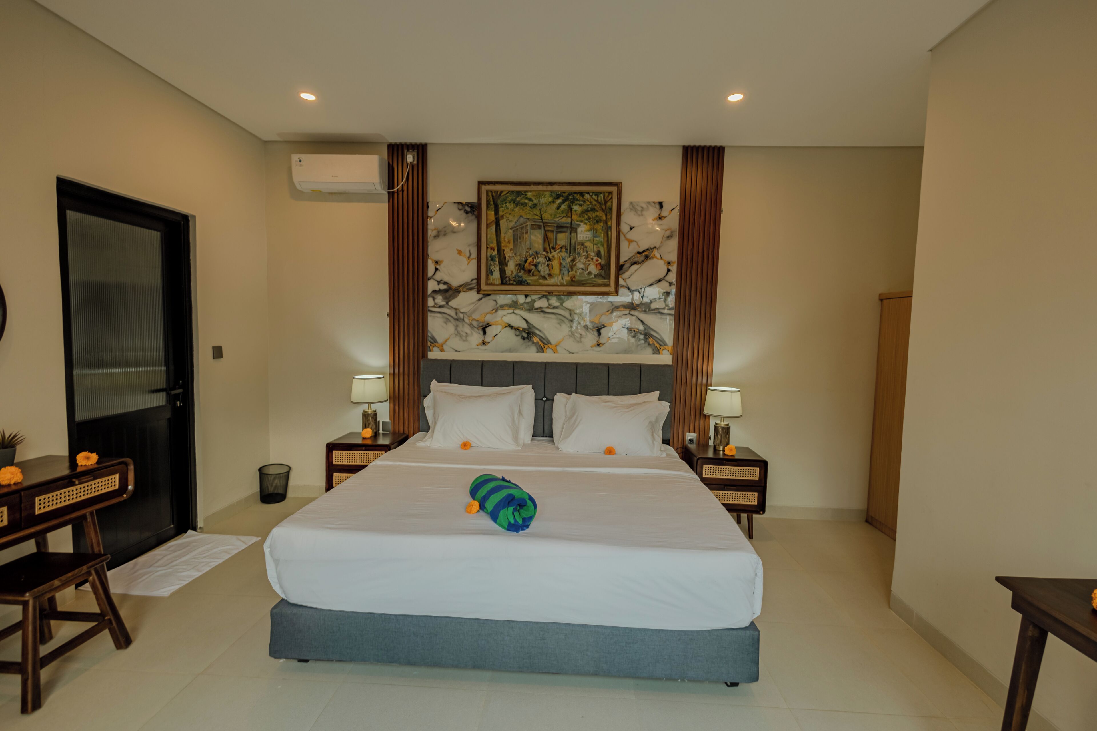 Habitación de hotel con cama, dos mesitas de noche, escritorio, silla, puerta y unidad de aire acondicionado.