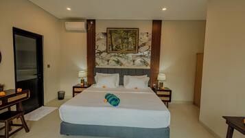 Habitación de hotel con cama, dos mesitas de noche, escritorio, silla, puerta y unidad de aire acondicionado.