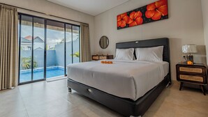 A hotel room with a large bed, a sliding glass door to a pool, a painting of flowers, and a nightstand with a lamp. - Shrivatsa Home Villa (Munggu)