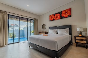 A hotel room with a large bed, a sliding glass door to a pool, a painting of flowers, and a nightstand with a lamp.