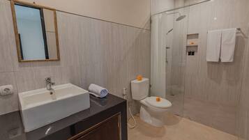 A modern bathroom with a sink, mirror, toilet, and shower area.