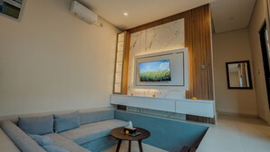 A modern living room with a sectional sofa, a small round table, a mounted TV, and a built-in cabinet with a marble accent wall. - Shrivatsa Home Villa (Munggu)