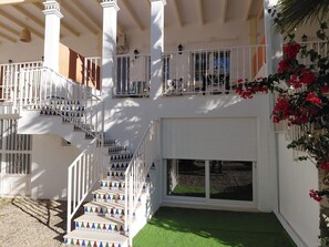 A multi-level building with white railings, a staircase with colorful tree decorations, and a balcony with red flowers.
