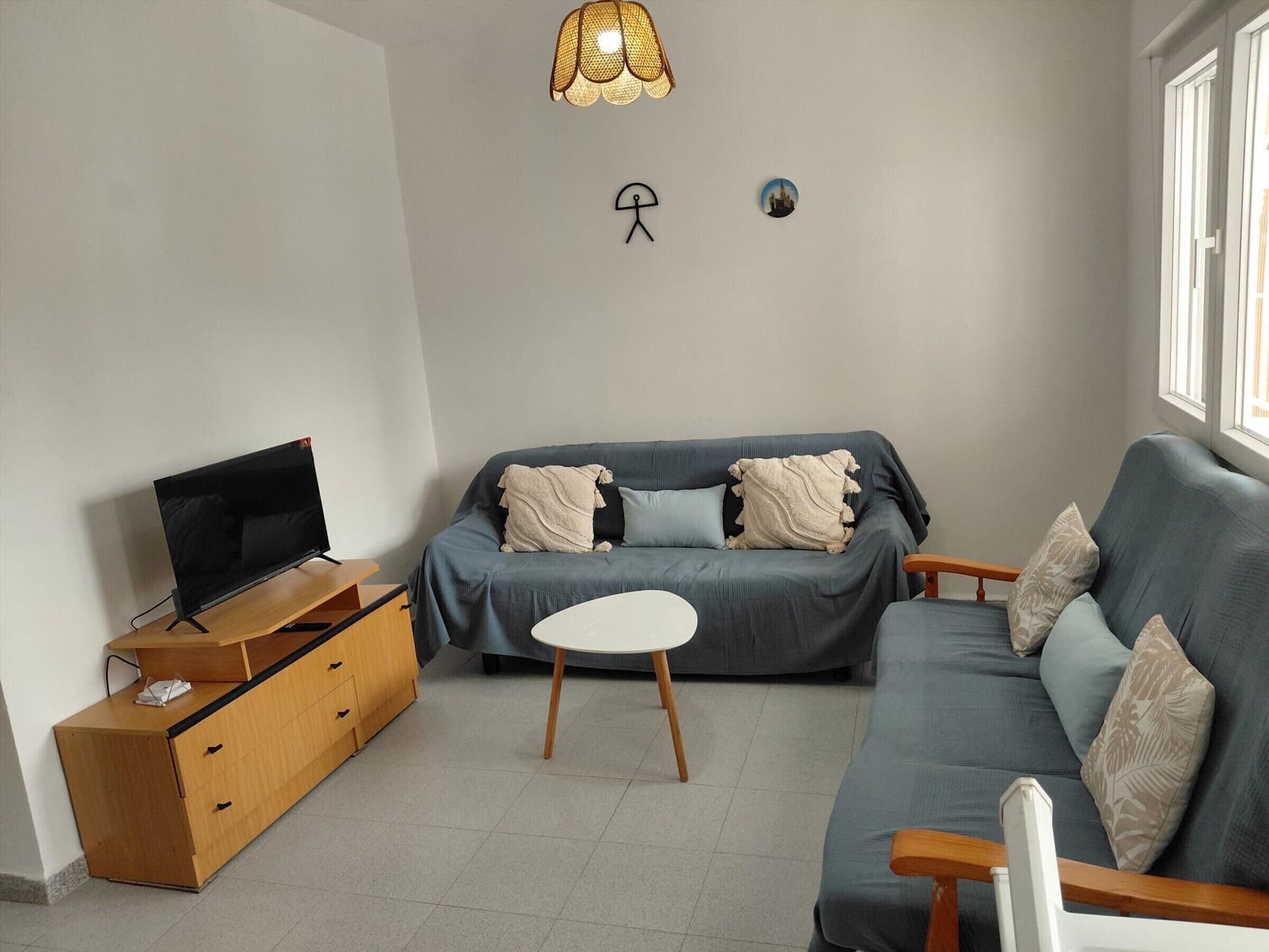 Una sala de estar con un sofá, un televisor sobre un soporte de madera, una mesita y una lámpara fijada a la pared.