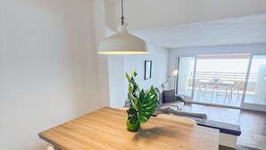 Un coin repas avec une table en bois, des chaises blanches, une suspension et une plante en pot.