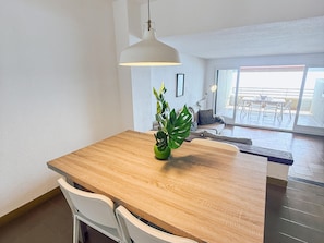 A dining area with a wooden table, white chairs, a hanging pendant light, and a potted plant. - Spacious apartment with sea view - 6 guests (Platja d'Aro)