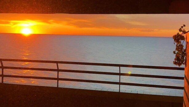 Un coucher de soleil sur l’océan, vu depuis un balcon doté d’une balustrade.
