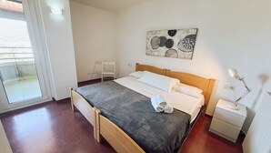 Une chambre à coucher avec un lit, une table de chevet avec une lampe, une chaise, un tableau au mur et une porte-fenêtre coulissante.