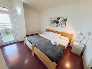 A bedroom with a bed, a bedside table with a lamp, a chair, a painting on the wall, and a sliding glass door. - Spacious apartment with sea view - 6 guests (Platja d'Aro)