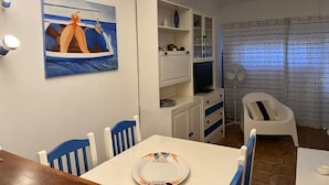Een eetgedeelte met een tafel, stoelen, een schilderij, een televisie en een ventilator.