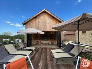 A wooden building with a balcony, outdoor seating, and umbrellas. - Renovated cottage with air conditioning - 4 guests (Savignac-de-Miremont)