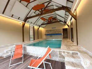 Ein Hallenbad mit Holzbalkendecke, gefliestem Boden und zwei orangefarbenen Liegestühlen.