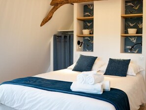 Ein Hotelzimmer mit einem Bett, zwei Kissen, einer blauen Tagesdecke und einem an der Wand befestigten Regal mit Dekoration.