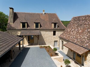 Un bâtiment en pierre doté d’une cour, de nombreuses fenêtres et d’un toit recouvert de tuiles.