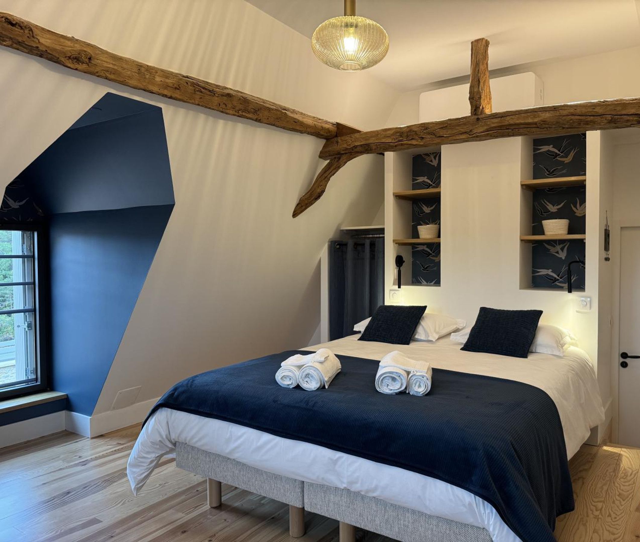 A bedroom with a bed, a window, and a wooden beam structure.