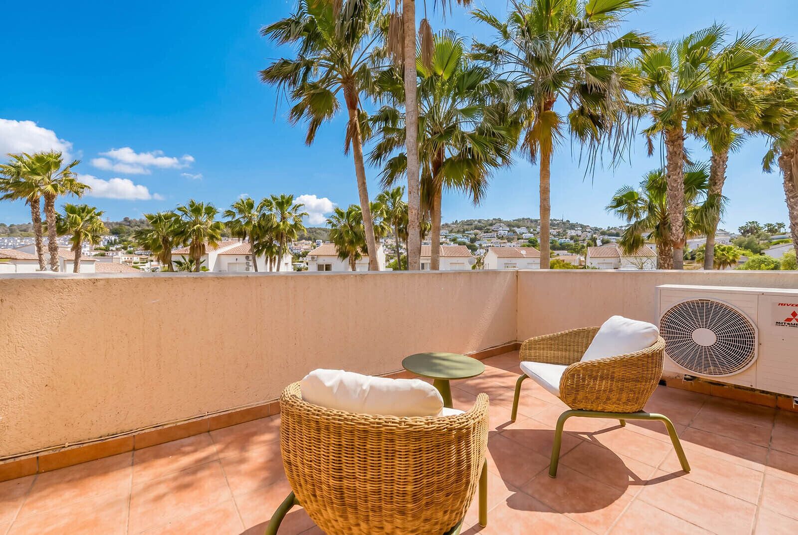 Een terras op het dak met rieten stoelen, een kleine tafel en een airconditioning.