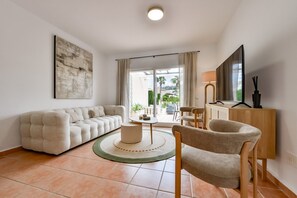 Ein Wohnzimmer mit einer Couch, einem Sessel, einem Couchtisch und einem Fernseher auf einer Holzkommode.