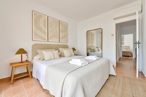 Ein Schlafzimmer mit Bett, Nachttischlampen, einem Spiegel und Blick in einen anderen Raum.