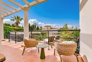 Ein Balkon mit Korbmöbeln, einem kleinen Tisch und Blick auf ein Gebäude sowie Grünflächen.