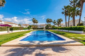 Une piscine à l’eau d’un bleu cristallin, entourée d’une pelouse bien entretenue et de palmiers.