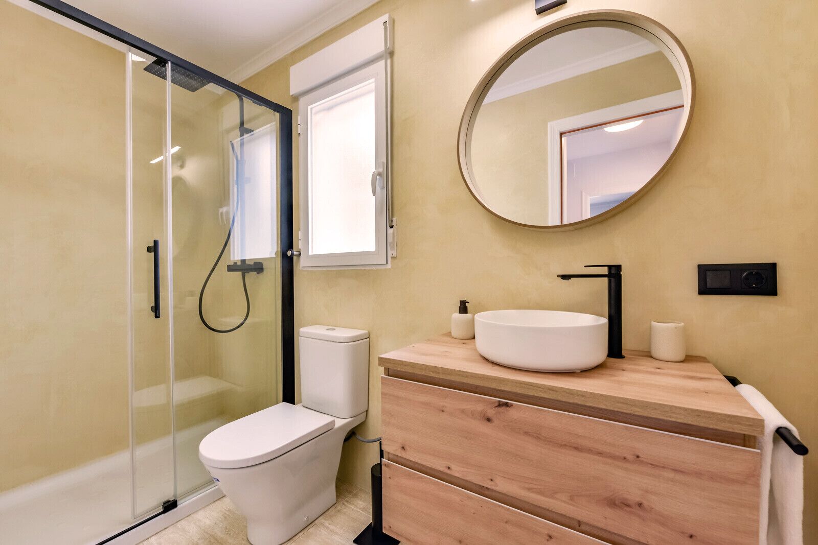 Een badkamer met een douchecabine van glas, toilet, wastafel met spiegel en een houten wastafelmeubel.