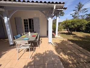 A covered patio with a table set for dining, outdoor chairs, and a pergola structure. - Calm villa in Cap-Ferret - 7 guests (Lège-Cap-Ferret)