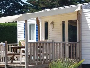 Une maison mobile de plain-pied dotée d’un porche couvert, d’une table de pique-nique et d’un petit espace jardin.