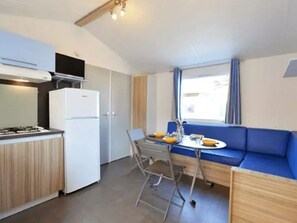 Eine kleine Küche mit Herd, Kühlschrank und Essbereich mit blauem Sofa und Tisch.