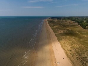 Ein Luftbild eines Strandes mit einer weiten Sandfläche, einigen Personen und einer fernen Küstenlinie.